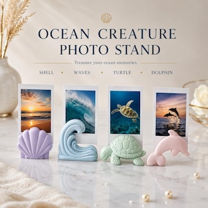 Puede incluir: Soporte para fotos Ocean Creature con soportes para fotos en forma de concha, ola, tortuga y delfín. Cada soporte contiene una foto con una escena oceánica. Los soportes para fotos son de colores pastel: lavanda, azul claro, verde menta y rosa.