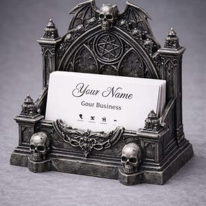 May include: Gothic-style business card holder in a dark gray finish. The holder features a skull and bat wing design, with the text "Your Name" and "Gour Business" on the cards. The holder is made of a durable material.