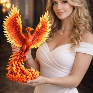 May include: A vibrant, orange and yellow phoenix sculpture with outstretched wings. The detailed artwork features a fiery design, showcasing the mythical bird's feathers and form. The sculpture is held in front of a blurred background.