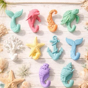May include: A set of 9 coastal hooks featuring various marine-themed shapes including a mermaid tail, dolphin, octopus tentacle, sea turtle, coral, starfish, anchor, whale tail, and two different seashells in pastel colors with the text Set of 9 COASTAL HOOKS.