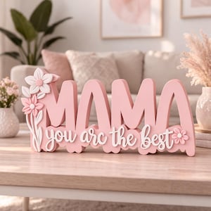 Może przedstawiać: Różowy drewniany znak z napisem "MAMA" dużymi literami i frazą "you are the best" w białym kolorze. Ozdobiony białymi i różowymi kwiatami.