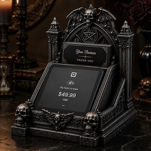 Puede incluir: Un soporte para terminal de pago de estilo gótico en gris oscuro con detalles arquitectónicos intrincados, incluyendo arcos apuntados, alas de murciélago y tres calaveras esculpidas. Sostiene una pantalla digital con 49,99 $ USD y una tarjeta que dice "Your Business THANK YOU."