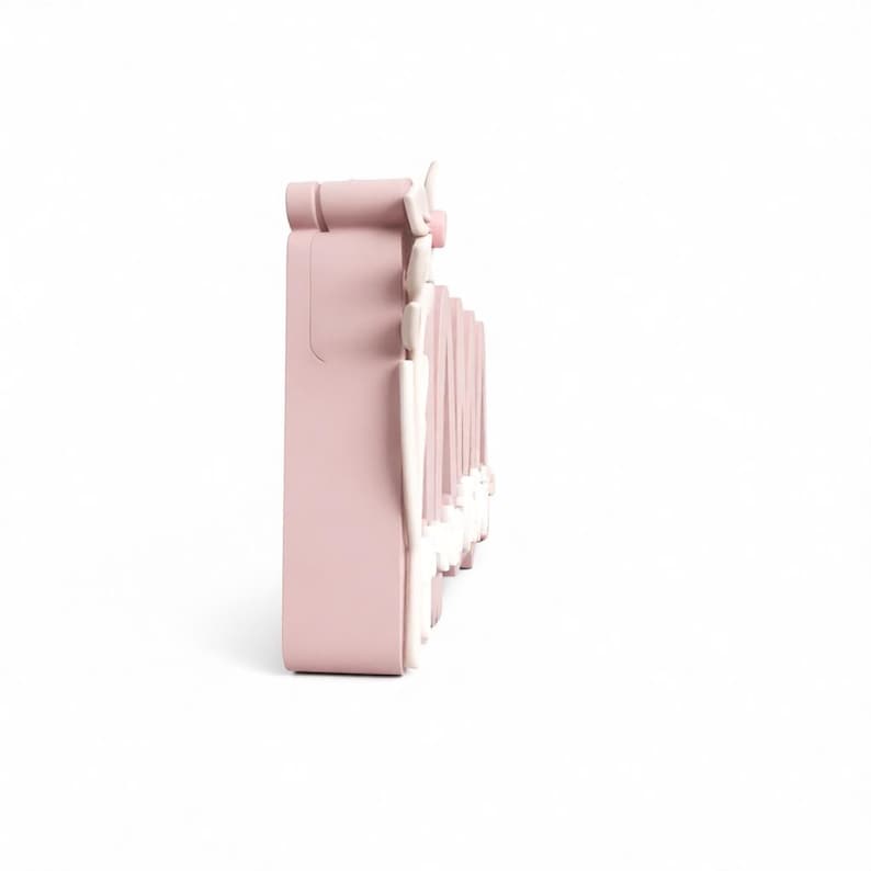May include: A light pink, decorative wall shelf with a detailed, ornate design. The shelf has a rectangular shape with a series of vertical, white accents. The shelf is designed to be mounted on a wall and is likely used for displaying small items.