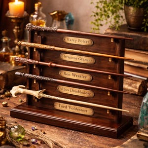 K&ouml;nnte beinhalten: Ein dunkler Holzst&auml;nder mit f&uuml;nf Zauberst&auml;ben, die jeweils mit einem Namen aus der Harry-Potter-Reihe beschriftet sind: Harry Potter, Hermine Granger, Ron Weasley, Albus Dumbledore und Lord Voldemort. Die Zauberst&auml;be sind in verschiedenen Braun- und Beiget&ouml;nen gehalten.
