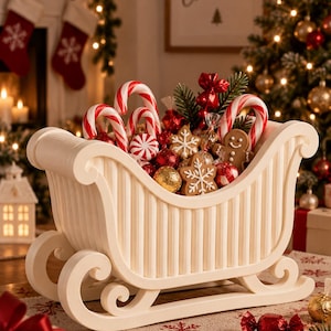 Puede incluir: Un trineo decorativo de color crema lleno de dulces navideños variados, que incluyen bastones de caramelo rojos y blancos, galletas de jengibre con forma de copos de nieve y un muñeco de jengibre, y varios chocolates envueltos en papel aluminio.