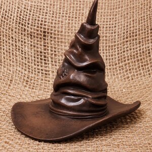 May include: A brown, sculpted hat with a wide brim and a tall, pointed top. The hat has a textured appearance and a small emblem on the side. The hat is likely a decorative item or a collectible.