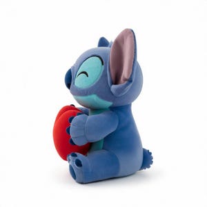 May include: A plush blue Stitch character from Lilo & Stitch, holding a red heart. The toy has large ears, a happy expression, and is sitting down. The plush toy is made of soft material.