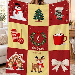 May include: A plush throw blanket featuring a grid of nine Christmas-themed illustrations including a snowman, a tree, a stocking, a mitten, an ornament, a wreath with the letter t, a mug, a gingerbread house, a reindeer, and a bow.