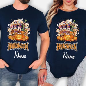 May include: A navy blue t-shirt featuring a graphic of Disney characters including Mickey Mouse, Minnie Mouse, Donald Duck, and Goofy in Halloween costumes sitting on pumpkins, with the text "HALLOWEEN" and a placeholder for a custom name.