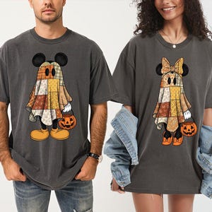 以下が含まれることがあります： ハロウィーンをテーマにしたグラフィックが描かれたチャコールグレーのTシャツ2枚。左のTシャツには、パッチワーク柄のシーツを被ったゴースト姿のキャラクターがカボチャのバケツを持っている様子が描かれています。右のTシャツには、リボンをつけたゴースト姿のキャラクターが描かれています。
