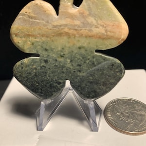 May include: A four-leaf clover-shaped stone sculpture with a mix of green, tan, and white colors. The clover is displayed on a clear plastic stand. A US quarter is next to the clover for size comparison. The text "C-200-105" is on a white label.