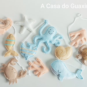May include: A felt ocean-themed mobile with a blue octopus, a yellow fish, a blue whale, a brown sea turtle, a pink coral, a brown seashell, a pink starfish, a brown crab, and a pink seahorse.