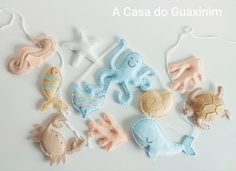 May include: A felt ocean-themed mobile with a blue octopus, a yellow fish, a blue whale, a brown sea turtle, a pink coral, a brown seashell, a pink starfish, a brown crab, and a pink seahorse.