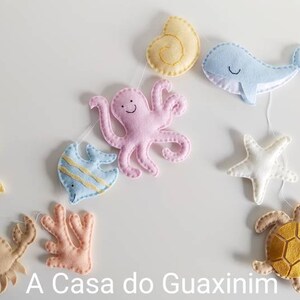 May include: A felt garland with a variety of sea creatures, including a seahorse, fish, octopus, starfish, turtle, and coral. The garland is strung on a white cord and is perfect for a nursery or child's room.