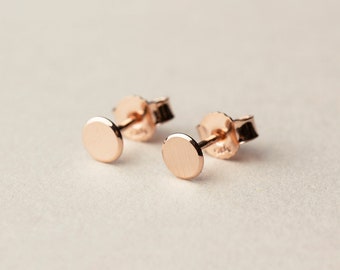 May include: A pair of small, round, rose gold stud earrings. The earrings are simple and elegant.