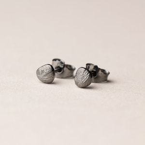 Könnte beinhalten: Ein Paar kleine, silberne Ohrstecker mit einem strukturierten, kieselsteinartigen Design.