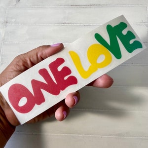 May include: A sticker with the words "ONE LOVE" in red, yellow, and green lettering. The letters are stylized and have a rounded, bubbly appearance.