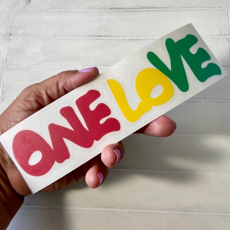 May include: A sticker with the words "ONE LOVE" in red, yellow, and green lettering. The letters are stylized and have a rounded, bubbly appearance.