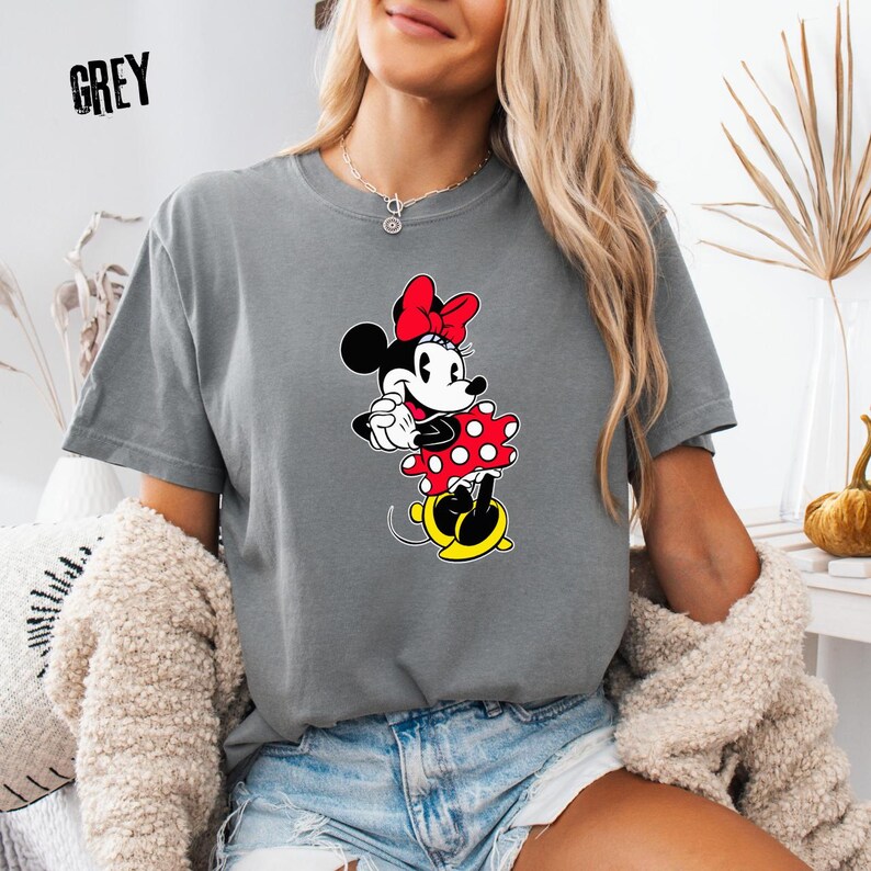 May include: Grey t-shirt featuring a Minnie Mouse graphic. The graphic shows Minnie Mouse wearing a red bow and a red polka dot dress. The word "GREY" is printed in the upper left corner of the shirt.