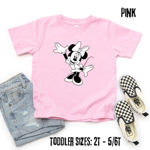 Peut inclure: T-shirt rose pour enfant avec un motif Minnie Mouse noir et blanc. L'image comprend un short en jean et des chaussures Vans &agrave; carreaux. Le t-shirt porte l'inscription "PINK" et "TODDLER SIZES: 2T - 5/6T".