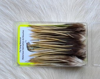May include: A clear plastic container filled with a variety of brown, tan, and white feathers. The container has a label that reads "Fly Tying Material Materiaux Fabrication de Mouches".