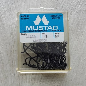 May include: A clear plastic box containing 50 black Mustad Limerick fishing hooks. The box has a blue label with the text "Mustad", "D. Mustad & Son A/S - Gjøvik, Nor", "Qual. 36990", "No. 2", "Qty. 50", and "Limerick". The label also includes the text "Made in Norway" and "Fabriqué en Norvège".