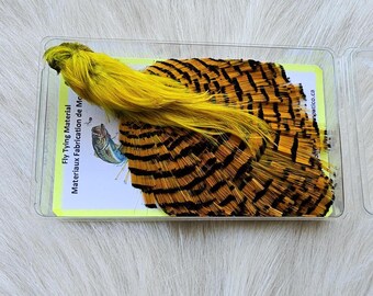 May include: A close-up of a fly tying material package containing a yellow feather and a set of black and gold feathers. The package is labeled "Fly Tying Material" and "Materiaux Fabrication de Mouches".
