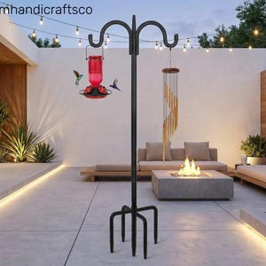 May include: A black metal bird feeder stand with a red hummingbird feeder and a wind chime. The stand has a four-pronged base and curved hooks for hanging items. The hummingbird feeder is red with a black base. The wind chime is made of wooden and metal elements.