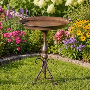 May include: A bronze-colored metal birdbath featuring a wide, shallow circular basin with two small bird figurines perched on the rim. The basin is supported by a slender, curved pedestal stand that rests on a decorative three-legged metal base.