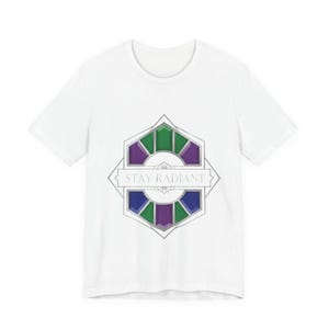 Puede incluir: Camiseta blanca con un diseño geométrico con detalles en verde, morado y azul. El diseño incluye el texto "STAY RADIANT" en fuente plateada, creando un gráfico elegante y llamativo.