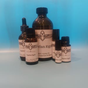May include: A collection of brown glass bottles and vials of varying sizes, labeled with the text "Egyptian Kyphi" and an illustration. The bottles are filled with a liquid, and some have black droppers or rollerball applicators. The background is a solid light blue.