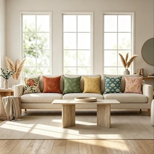 May include: A set of six square throw pillows arranged on a beige sofa. The pillows feature various designs including a large floral print, solid rust orange, green with leaf patterns, solid yellow, teal with lotus flowers, and pink with botanical motifs.