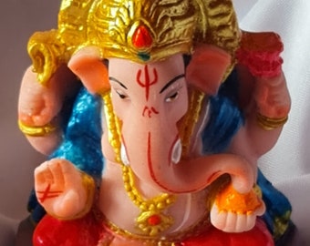 May include: A colourful statue of the Hindu deity Ganesha. The statue is made of painted plaster and depicts Ganesha sitting with his trunk raised and holding a sweet in his hand. He is wearing a blue and red robe and a gold crown.