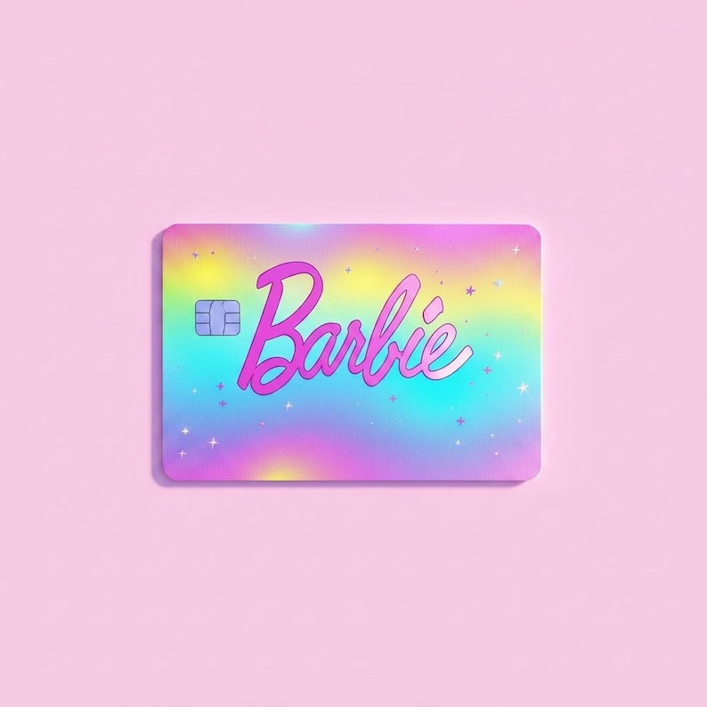 May include: A rectangular payment card featuring a vibrant holographic gradient background that shifts from yellow to blue and pink. The word Barbie is printed in a bold pink script font across the center, accented by small white star icons.