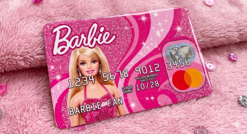 K&ouml;nnte beinhalten: Ein rechteckiger, pinkfarbener Kreditkartenaufkleber mit Glitzereffekt und Barbie-Logo. Das Design zeigt eine blonde Puppe in einem pinken Kleid, den Text BARBIE FAN, die Nummer 1234 5678 9012 3456, das Datum GOOD THRU 10/28 und ein rundes Logo.