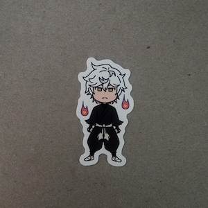 May include: A sticker featuring a chibi-style character with white hair, wearing a black outfit with a white belt. The character has a serious expression and is flanked by two small flames. The sticker is on a gray background.