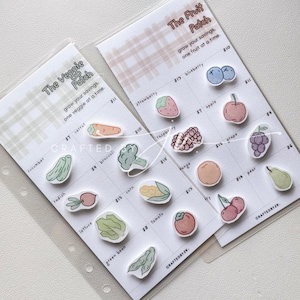 May include: Two illustrated cards, "The Veggie Patch" and "The Fruit Patch," feature colorful stickers of vegetables and fruits with prices. The cards are in clear plastic sleeves. The text "CRAFTEDBYJV" is visible.