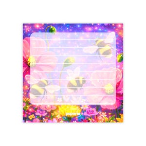 May include: A notepad with a floral and bee design. The background is a vibrant mix of pink, purple, and blue, with a field of flowers and several bees. The notepad has lined pages and the word "paperie" is visible.