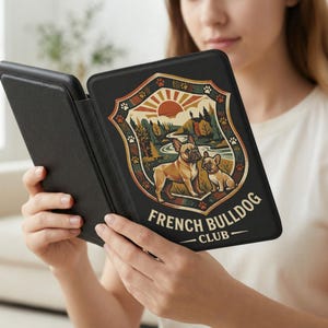 May include: Black e-reader cover featuring a graphic of two French Bulldogs in a nature scene with a rising sun. The text "FRENCH BULLDOG CLUB" is displayed below the image. The cover is open, revealing the screen.
