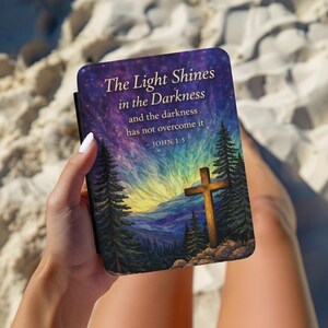 May include: A book cover with the text "The Light Shines in the Darkness" and a cross illustration. The background features a starry sky, mountains, and pine trees. The text "- JOHN 1:5" is also included.