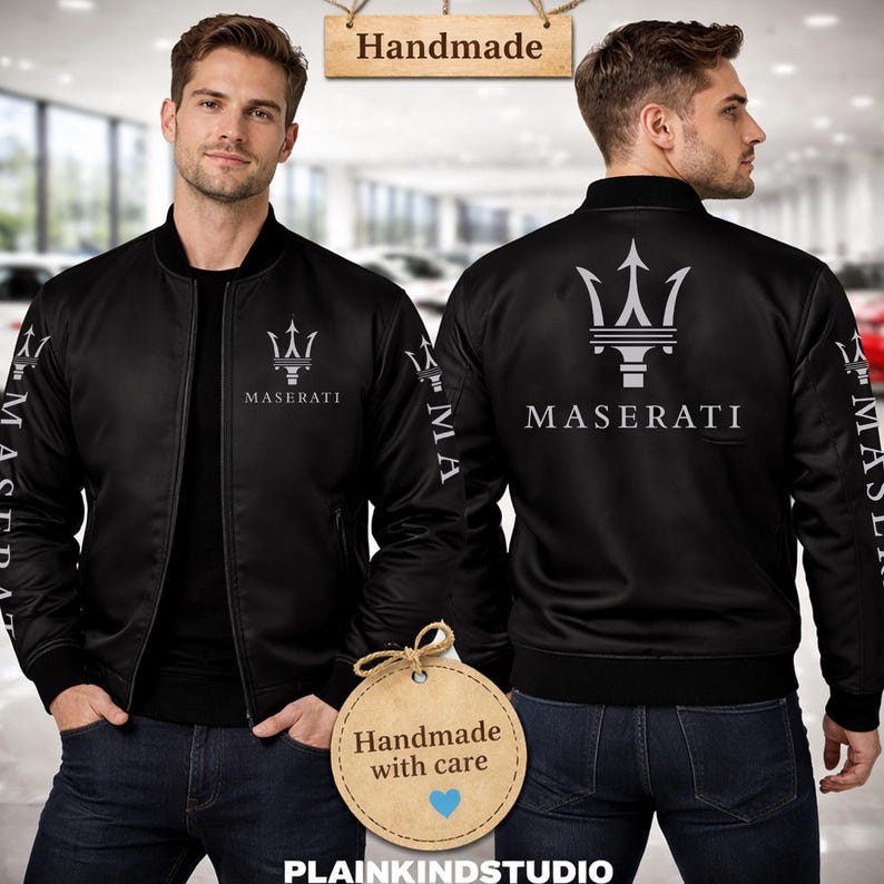 May include: A black bomber jacket featuring the silver Maserati trident logo and text on the chest and sleeves. The jacket has a ribbed collar, cuffs, and hem. A wooden sign above reads Handmade, and a circular tag below reads Handmade with care.
