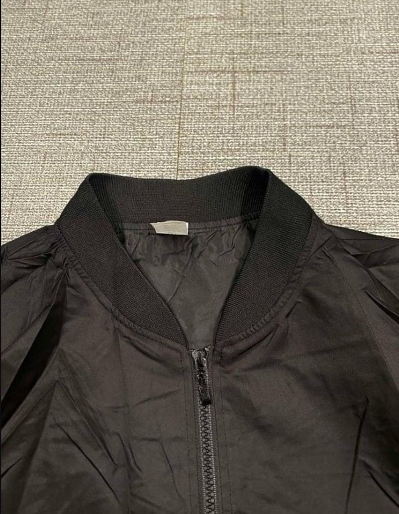 May include: A black bomber jacket with a ribbed collar and cuffs. The jacket has a full zipper closure down the front. The fabric appears to be a lightweight material, suitable for layering. The jacket is a classic style.