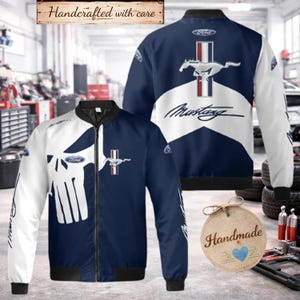 Peut inclure: Un blouson aviateur bleu marine et blanc arborant un grand motif de crâne blanc sur le devant, un logo Ford et un emblème Mustang. Le dos présente un logo Ford, un graphique Mustang avec un cheval au galop et une bande rouge, blanche et bleue.
