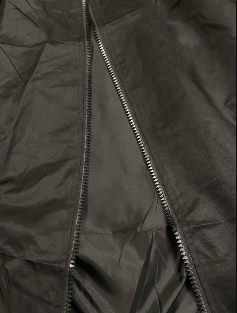 May include: Close-up of a black jacket with a zipper. The jacket appears to be made of a smooth, possibly water-resistant material. The zipper runs down the center, partially open, revealing the interior lining.