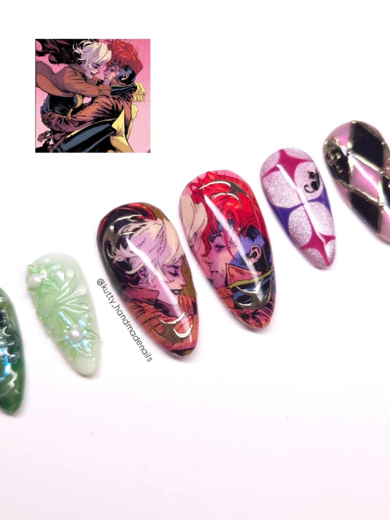 May include: A collection of artificial nails with various designs. Some nails feature comic book art of two characters embracing, while others have abstract patterns in pink, purple, and silver. One nail is green with a floral design.