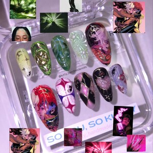 May include: A collection of custom-designed, long, oval-shaped artificial nails. The nails feature various designs, including comic book art, glitter, and abstract patterns in colors like red, pink, black, and green. Some nails have a glossy finish, while others have a matte appearance.