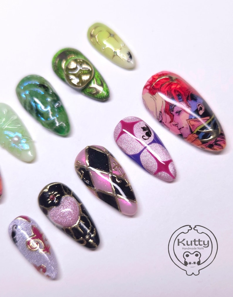 May include: A collection of artificial nails with various designs. The nails feature a range of colors, including green, pink, black, and purple, with gold accents. Some nails have intricate patterns, while others display cartoon-style illustrations. The "Kutty Handmade Nails" logo is visible.