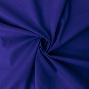 May include: A close-up shot of a deep indigo fabric with a subtle sheen. The fabric is gathered and swirled, creating soft folds and shadows. The color is a rich, saturated blue, and the texture appears smooth and lightweight. The overall effect is elegant and luxurious.