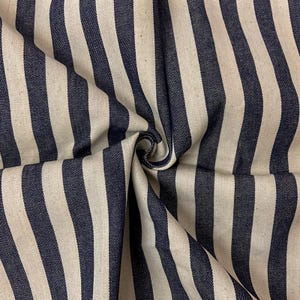 May include: A piece of fabric featuring a repeating pattern of vertical stripes in dark navy blue and off-white. The textile is gathered in the center, creating soft folds and shadows that highlight the texture and the consistent stripe width.
