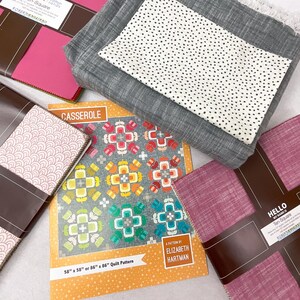 May include: A collection of quilting supplies, including fabric bundles in various colors and patterns, and a quilt pattern book titled "CASSEROLE" by Elizabeth Hartman. The quilt pattern is for a 58" x 58" or 86" x 86" quilt.